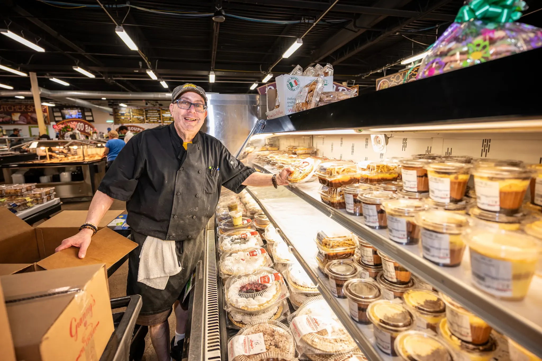 A baker at the bakery case with pies, cannoli and cheesecakes