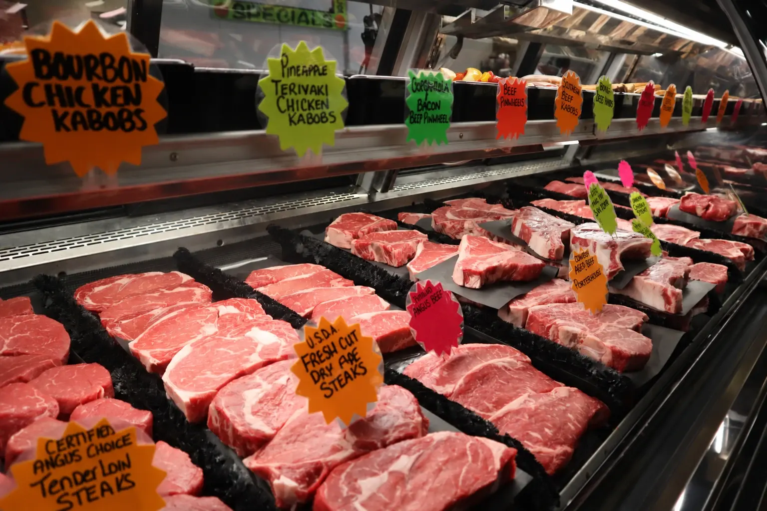 The butcher case stocked with steaks and kabobs under hand-lettered signs