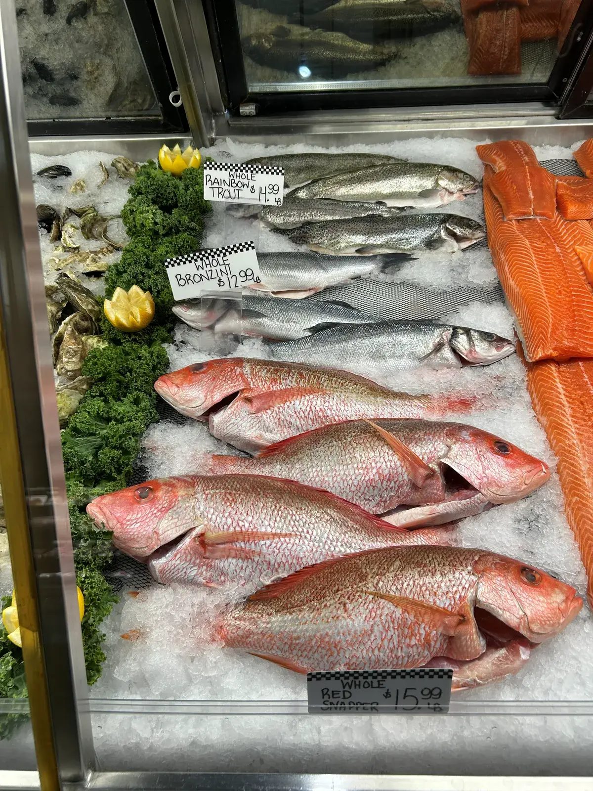Whole red snapper, bronzini and rainbow trout on ice with oysters and salmon fillets in the seafood case