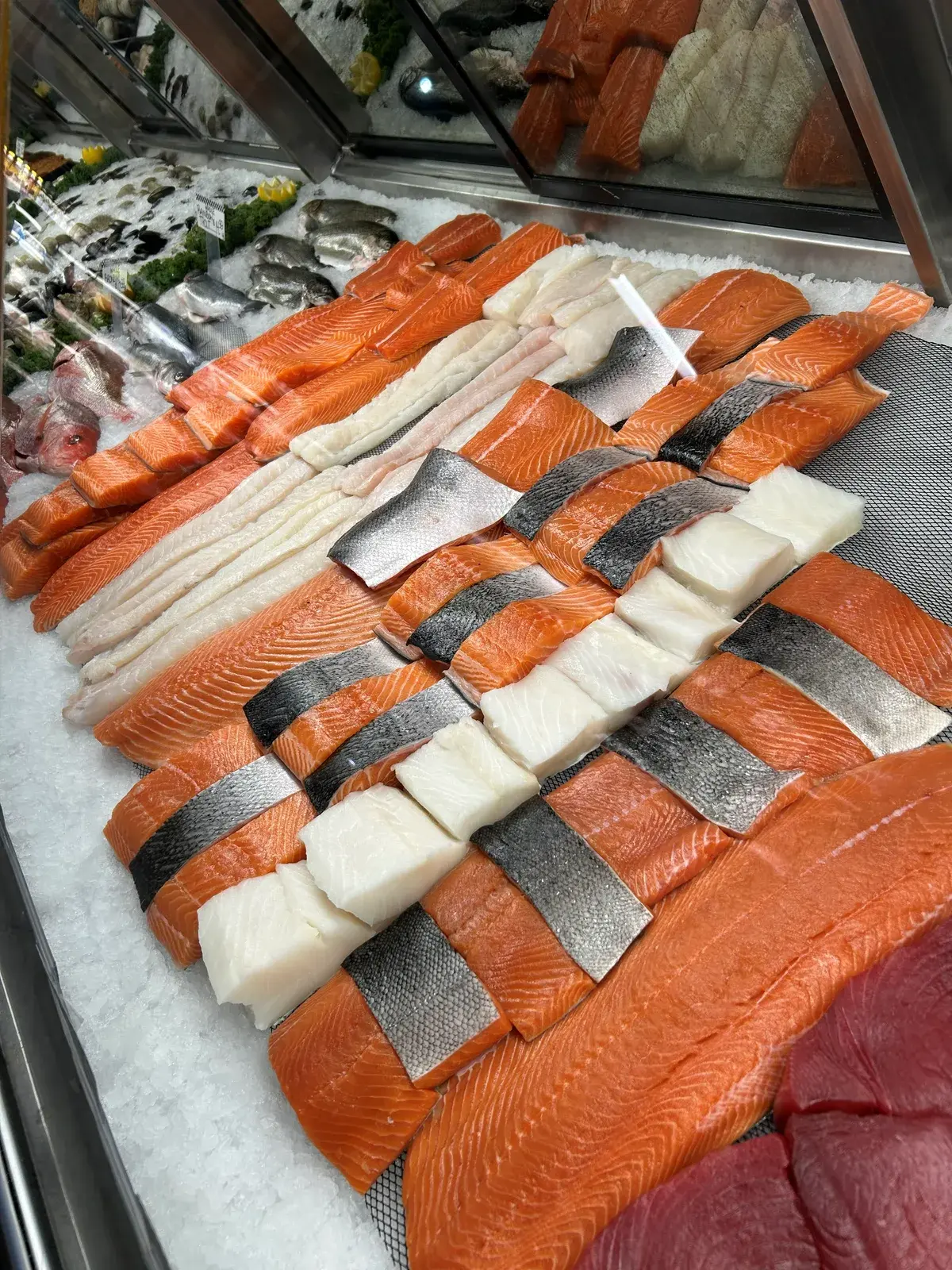 Salmon, cod and tuna fillets arranged in a woven lattice in the seafood case